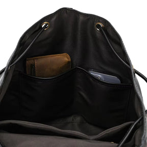 The Vintage Leather Backpack crafted from black cowhide leather displays its interior with two pockets. In one pocket rests a brown wallet, while a smartphone occupies the other. This stylish travel companion is equipped with a drawstring closure featuring gold grommets.