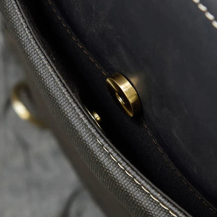 A close-up shot captures the interior snap button closure on the Leather Business Travel Briefcase Backpack, showcasing its metal components. The fine stitching along the edge highlights its well-made and sturdy design in textured dark genuine cowhide leather. Lifetime Warranty included. The softly blurred background enhances the focus on these details.