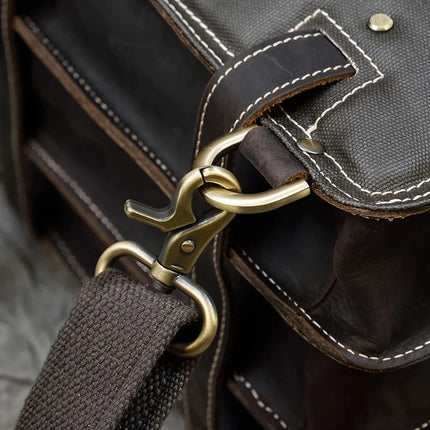 Close-up of the Leather Business Travel Briefcase Backpack in dark brown genuine cowhide leather, featuring white stitching and a metallic clasp fastening the adjustable shoulder strap to the bag. The image highlights the sturdy craftsmanship and detailed design of the bag's hardware and material.