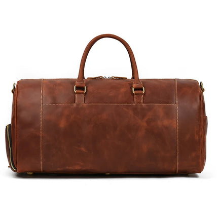 The Weekender 23 Leather Travel Bag is a large brown travel bag crafted from genuine cowhide leather that boasts a smooth texture. It features two sturdy handles on top, brass hardware, and white stitching along the seams. The bag also includes a zippered shoe compartment on one side and a spacious main compartment.