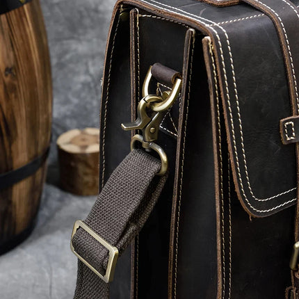 A detailed view of the Leather Business Travel Briefcase Backpack reveals its dark brown genuine cowhide leather exterior with white stitching. The bag features a metal clasp and adjustable gray strap, positioned against a wooden barrel that highlights its rustic appeal. Included is a lifetime warranty for added assurance.