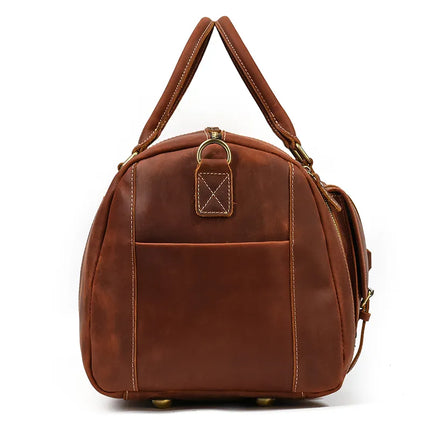 The Weekender 23 Leather Travel Bag is crafted from genuine cowhide leather in a rich brown color and features two handles and brass hardware. It boasts a front pocket, rounded edges, and visible stitching that enhances its simple yet elegant design. Additionally, it includes a shoe compartment and small metal feet for added support.