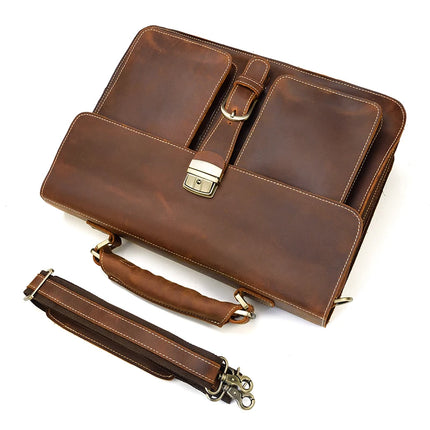 The Leather 16" Business Briefcase is made from genuine cowhide leather and features a brown exterior with two front pockets, a central buckle, and a metal clasp. It comes equipped with a padded handle and an adjustable, detachable shoulder strap, which is displayed separately lying in front of the briefcase.