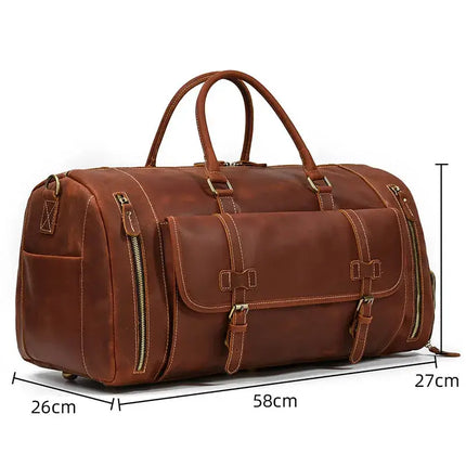 The Weekender 23 Leather Travel Bag is a brown travel bag crafted from genuine cowhide leather. It features multiple zipper pockets and buckle straps, while also including a dedicated shoe compartment. Measuring 58cm in length, 27cm in height, and 26cm in width, the bag is displayed on a white background with two sturdy handles for easy carrying.