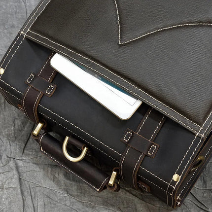A close-up image of a Leather Business Travel Briefcase Backpack made from dark brown genuine cowhide leather with beige stitching and brass hardware. The bag is partially open, revealing a white electronic device inside, possibly a tablet. It is placed on a crumpled grey fabric surface.