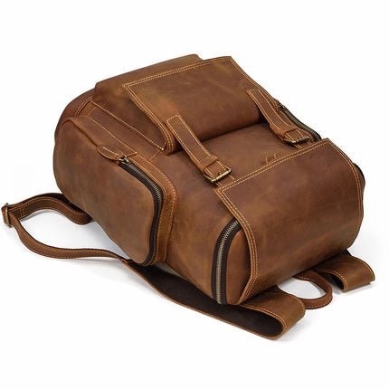 The Vintage Leather Travel Backpack, crafted from genuine cowhide leather, is displayed lying flat. It features multiple compartments and zippers, padded shoulder straps, and brass buckles. The visible stitching accentuates the high-quality craftsmanship of the bag, which also includes a dedicated laptop compartment. The background is pure white.