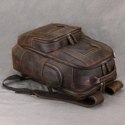 The Vintage Leather Travel Backpack is crafted from genuine cowhide leather and features multiple zipper compartments along with padded straps. It showcases a rugged, distressed texture with fine stitching details, making it perfect for carrying your travel essentials against a neutral gray fabric background.