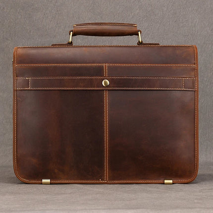 The Vintage Business Travel Briefcase is crafted from genuine leather and boasts a top handle and brass hardware, including a clasp and corner protectors. Its sleek, simple design with visible stitching features an adjustable strap for added convenience. Inside, there’s a dedicated compartment to keep your laptop secure. The briefcase is showcased against a plain, grey background.