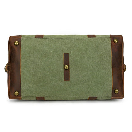 The image displays the bottom view of a vintage green fabric and genuine leather Canvas & Leather Travel Duffle. It features brass feet and accents, sturdy leather straps, and a central brass stud, combining style with durability for your adventures.