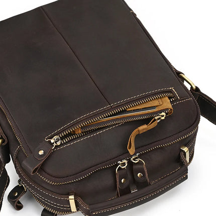 The Dark Brown Leather Shoulder Bag, crafted from genuine cowhide leather, boasts multiple compartments. This shoulder bag features a tan zipper pull on the front zipper pocket, along with additional rivets and alloy hardware. The lighter-colored stitching offers a contrasting detail to the design.