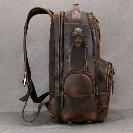 The Vintage Leather Travel Backpack is displayed from a side view against a plain gray background. This genuine cowhide leather backpack boasts multiple zippered compartments, adjustable shoulder straps, and a subtle buckle detail on the front pocket. The leather showcases a slightly worn, timeless appearance.
