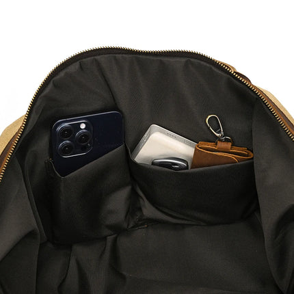 Inside the Canvas & Leather Travel Duffle, a black smartphone is in one pocket, and a white power bank with a brown leather wallet sporting a keychain fits snugly in another. The dark lining contrasts elegantly with the gleaming gold zipper.