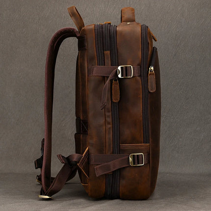 A side view of the Vintage Leather Travel Backpack, crafted in genuine brown leather, showcases metal buckles, zippers, and adjustable straps. It rests against a gray background and features multiple compartments for storage, making it an ideal men's accessory.