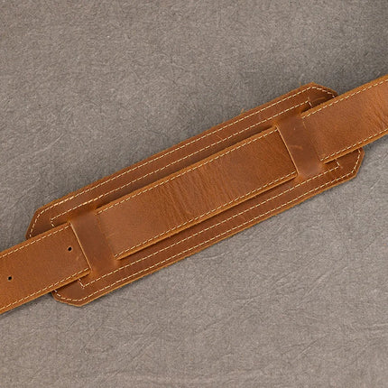 A brown genuine cowhide leather vintage shoulder bag with an adjustable buckle is laid flat on a textured gray background. The bag features reinforced stitching and a padded section for shoulder comfort, highlighting its practical benefits.