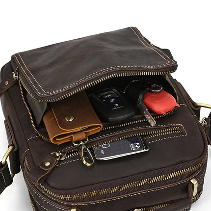 A Dark Brown Leather Shoulder Bag is partially unzipped and open at the top. Inside, a brown leather wallet, a set of car keys, and another bunch of keys with keychains are visible. The bag features detailed stitching and alloy hardware.