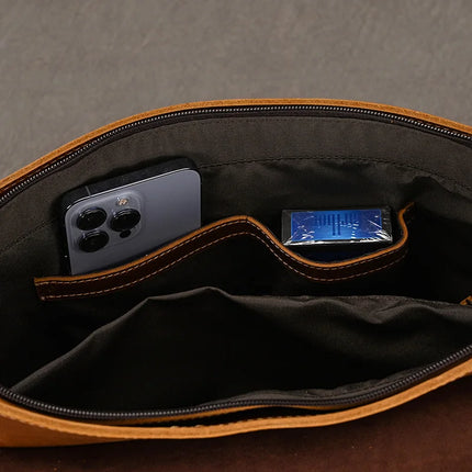 Interior view of the Vintage Leather Shoulder Bag in genuine cowhide leather, showcasing its practical benefits with two compartments. One holds a smartphone with multiple rear cameras, while the other contains a small blue package. The background is plain grey fabric.