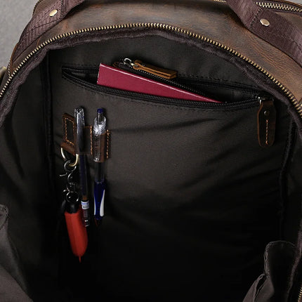 The interior of the Vintage Leather Travel Backpack reveals multiple compartments. A red notebook is partially zipped inside a pocket, while the front compartment houses several pens, a set of keys, and a flashlight. Crafted from genuine cowhide leather, the backpack features a dark lining adorned with leather accents and zippers.