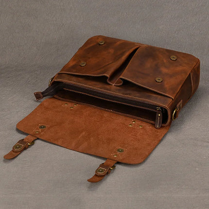 The Leather 14" Briefcase Shoulder Bag, in rich brown leather, opens to reveal a zipped compartment with the flap laid flat. Four brass snap buttons adorn the flap, and the bag boasts a worn, rustic aesthetic against a textured background—a perfect blend of professional style and genuine cowhide craftsmanship.