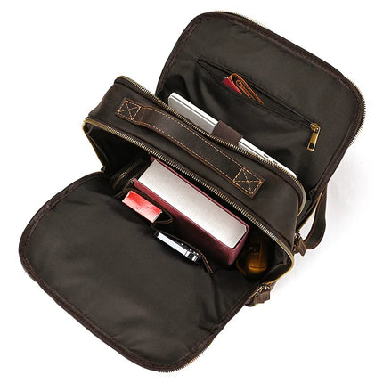 Open the Vintage Leather Daypack with two compartments. The front compartment contains a small red box, a phone, and a book, while the back compartment holds a tablet and some brown papers in a zippered pocket. The genuine cowhide leather backpack's interior is lined with fabric.