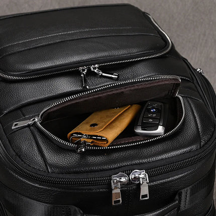 The Black Leather Travel Backpack, with a partially opened front pocket showcasing a tan leather wallet and a car key fob, features silver zippers and a spacious interior that suggests premium leather construction. The well-padded and high-quality backpack stands out against a plain gray background.