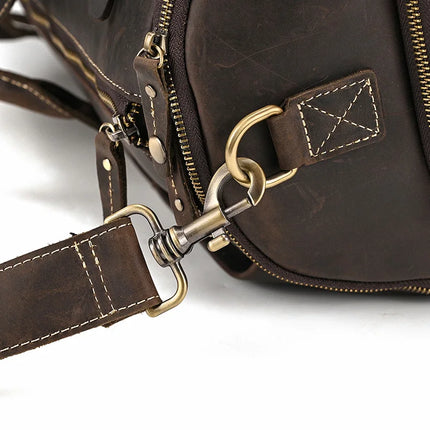 Close-up view of a Weekender 22 Leather Travel Duffle Bag made from genuine cowhide leather, showing detailed stitching, a brass-colored metal hook attached to a D-ring, and a zipper. The image emphasizes the craftsmanship and hardware of the bag's design.