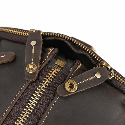 Close-up of a Weekender 22 Leather Travel Duffle Bag in genuine cowhide leather, showcasing its brass zippers and button details. The zippers are partially open, revealing the inner lining, while the visible stitching highlights the bag's craftsmanship and sturdy construction.