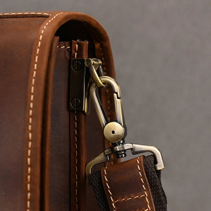 Close-up of the Vintage Business Travel Briefcase, made from genuine leather, featuring a brass zipper and an attached adjustable strap. The strap is connected to the briefcase with a metal clasp and rivet. The visible stitching on the leather showcases the craftsmanship. The background is a solid neutral color.