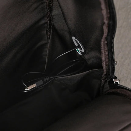 A close-up of the interior of the Black Leather Travel Backpack reveals a small compartment crafted from black fabric, featuring a USB cable with a standard connector plugged into an internal socket.