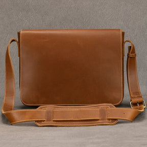 The Vintage Leather Shoulder Bag boasts a sleek design and smooth texture, crafted from genuine cow leather. It includes an adjustable shoulder strap with a comfortable shoulder pad and a plain flap closure. Set against a neutral gray surface, its timeless style is truly enhanced.