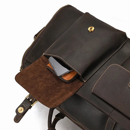 The Weekender 22 Leather Travel Duffle Bag, crafted from genuine cowhide leather in a rich dark brown color, features gold zippers and matching dark brown stitching. An open pocket reveals a smartphone partially tucked inside, while the interior is lined with lighter brown suede material, adding a touch of elegance to this versatile bag.