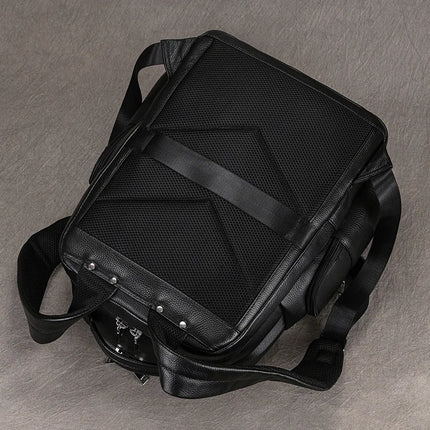 The **Black Leather Travel Backpack** is depicted from the back, showcasing its structured, rectangular design. It includes padded mesh adorned with horizontal and diagonal straps, black shoulder straps, and silver hardware positioned on the bottom left corner. The roomy interior provides ample storage space, all presented against a grey backdrop.