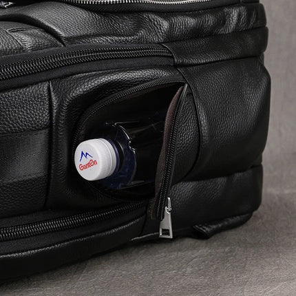 A Black Leather Travel Backpack featuring premium leather construction is shown with its zippered pocket partially open, revealing a water bottle inside. The bottle cap is adorned with the Ganjen logo and a blue mountain graphic. The backpack rests on a grey surface, suggesting the spacious interior it offers.