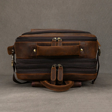 A vintage leather travel backpack, crafted from genuine leather with multiple compartments, two top handles, and zipper closures, is set against a plain gray background. The handmade backpack boasts a rugged, vintage look.