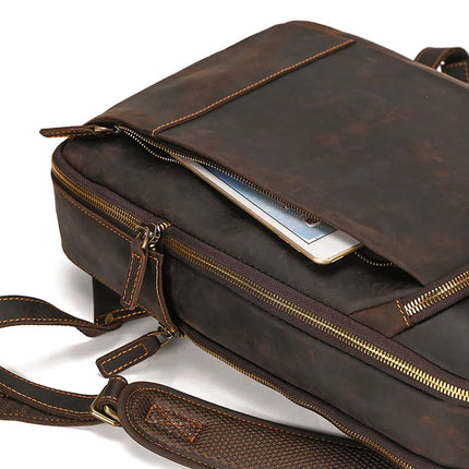 A close-up of the Vintage Leather Daypack, crafted from genuine cowhide leather, showcases its detailed stitching and sturdy metal zippers. One zipper compartment is slightly open, revealing a book or tablet partially inside. This vintage leather daypack features an adjustable strap equipped with a cushioned shoulder pad for added comfort.