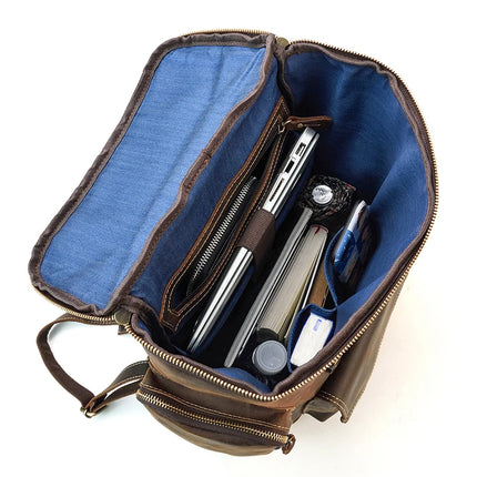 The Vintage Leather Travel Backpack, with its open design and blue interior lining, made from genuine cowhide leather, displays neatly organized contents such as a laptop in its dedicated compartment, notebooks, a water bottle, a pen, and a small pouch. The multiple compartments and zippers illustrate the backpack's capability for neat and efficient packing.