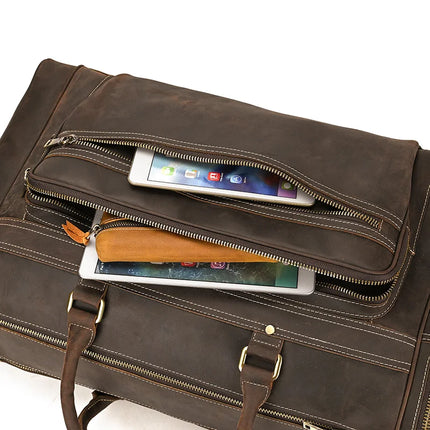 A brown genuine leather bag, the Luggage 24 Leather Travel Bag features two open zippers—one revealing a tablet and the other a smaller electronic device. The travel bag boasts visible stitching, brass hardware, and durable leather handles and straps.