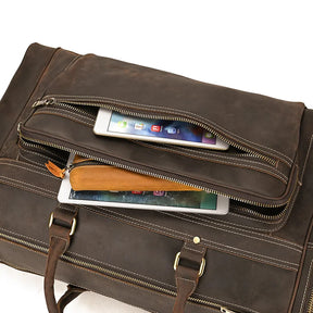 A brown genuine leather bag, the Luggage 24 Leather Travel Bag features two open zippers—one revealing a tablet and the other a smaller electronic device. The travel bag boasts visible stitching, brass hardware, and durable leather handles and straps.