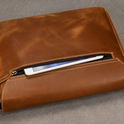 The Vintage Leather Shoulder Bag, crafted from genuine cowhide leather, showcases a zipper pocket partially open, revealing the edge of a tablet inside. The smooth, polished finish and visible stitching enhance its appeal. Offering practical benefits, it rests gracefully on a gray surface.