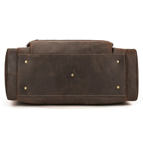 A brown genuine leather Luggage 24 Leather Travel Bag is shown from the bottom, highlighting its sturdy base with reinforced stitching. Four metal studs are visible on the bottom for added protection and durability. The material appears to be smooth and high-quality, making it perfect as a travel bag.