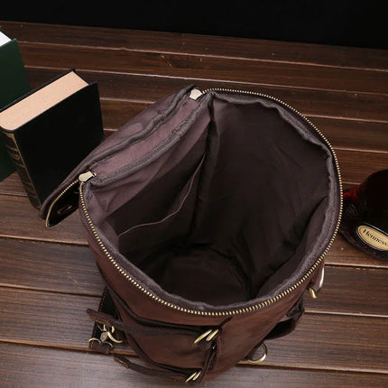 A stylish traveler's Vintage Leather Travel Backpack, made from genuine brown cowhide leather, rests on a wooden surface with its main compartment open, revealing a spacious interior with pockets. Nearby, a book and an Hennessy bottle enhance the versatile bag's allure.
