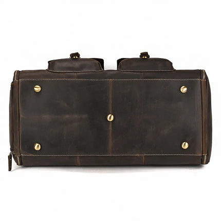 Bottom view of a dark brown Weekender 22 Leather Travel Duffle Bag with brass studs at the corners and center for support and protection. The genuine cowhide leather's texture and subtle stitching are visible, emphasizing the bag's craftsmanship and durability.