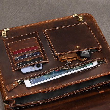 A Vintage Business Travel Briefcase with an adjustable strap sits open, showcasing various items inside. Credit cards are tucked into a designated pocket, alongside a smartphone and a car key. The briefcase also features a zippered compartment, partially unzipped to reveal a tablet or e-reader inside. It boasts brass accents and exudes a rustic charm.