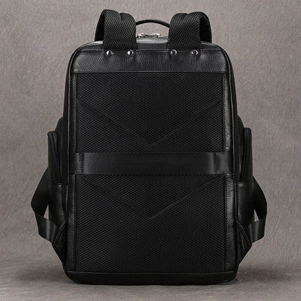 The Black Leather Travel Backpack is displayed against a gray background. It features a structured design with premium leather construction, a textured mesh back panel, adjustable shoulder straps, two side pockets, and a top handle. The backpack has silver stud accents near the top and boasts a sleek, modern look.