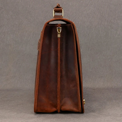 Side view of the Vintage Business Travel Briefcase, crafted from genuine leather and designed with two compartments, including a dedicated laptop compartment. The bag is adorned with brass hardware, featuring a clasp at the top and rings on either side. The smooth leather showcases visible seams and stitching, while an adjustable strap complements the design against a plain gray background.