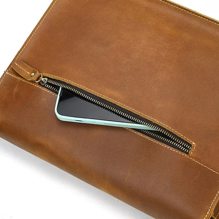 A close-up image of the Leather Business Travel Shoulder Bag, showcasing its genuine cowhide leather in a rich brown color. The high-quality alloy hardware is visible, as well as a partially open zipper pocket that reveals a light blue smartphone inside. The smooth leather features a slightly worn texture, adding to its charm.