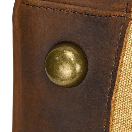 Close-up of a metallic circular button on the Canvas & Leather Travel Duffle, set against genuine leather on the left and beige fabric on the right, with visible stitching details.