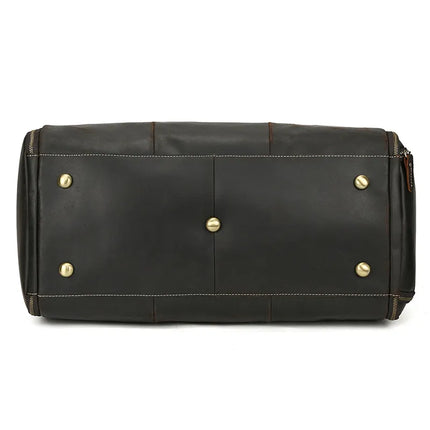 The image shows the bottom view of the Luggage 22 Leather Travel Duffle Bag, featuring four gold-colored durable alloy hardware studs and one central metal knob to protect the base from wear and tear. The bag also boasts brown stitching details along the edges.