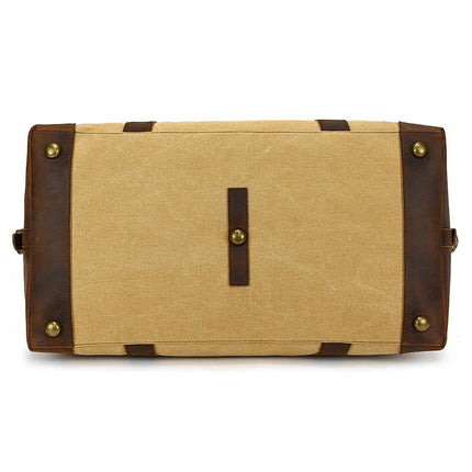 The image showcases the bottom view of a vintage Canvas & Leather Travel Duffle in beige, featuring four brass studs for stability and a horizontal leather strip. The brown genuine leather details on the sides and corners enhance its timeless charm.