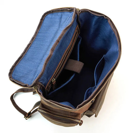 The Vintage Leather Travel Backpack, crafted from genuine cowhide leather, is displayed. The opened brown backpack showcases a blue fabric interior featuring visible compartments, a zippered pocket, and a padded laptop compartment. The bag is stylishly positioned on a white surface.