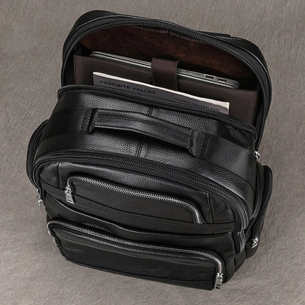 The Black Leather Travel Backpack is displayed standing upright with its top main compartment open, showcasing a laptop and a book titled "Yosemite Valley" inside. This premium leather bag features several zipped pockets and a top handle, merging style with functionality.
